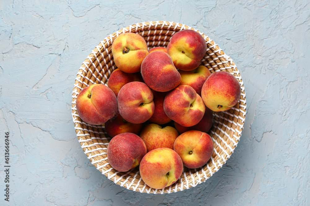 Wicker bowl with sweet peaches on blue background