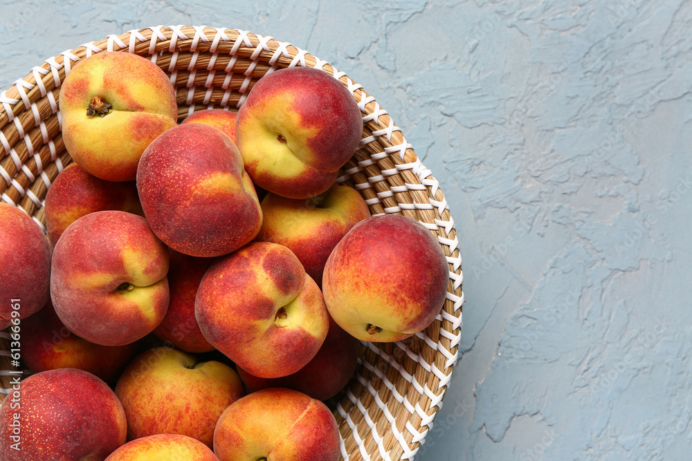 Wicker bowl with sweet peaches on blue background