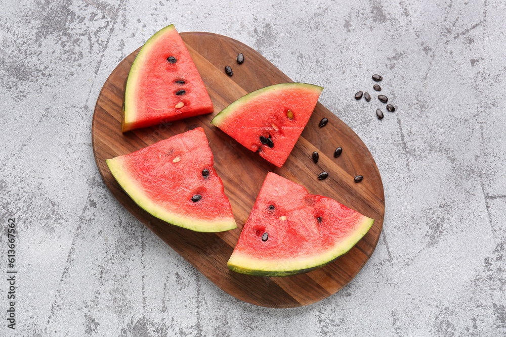 Board with pieces of fresh watermelon and seeds on grey background