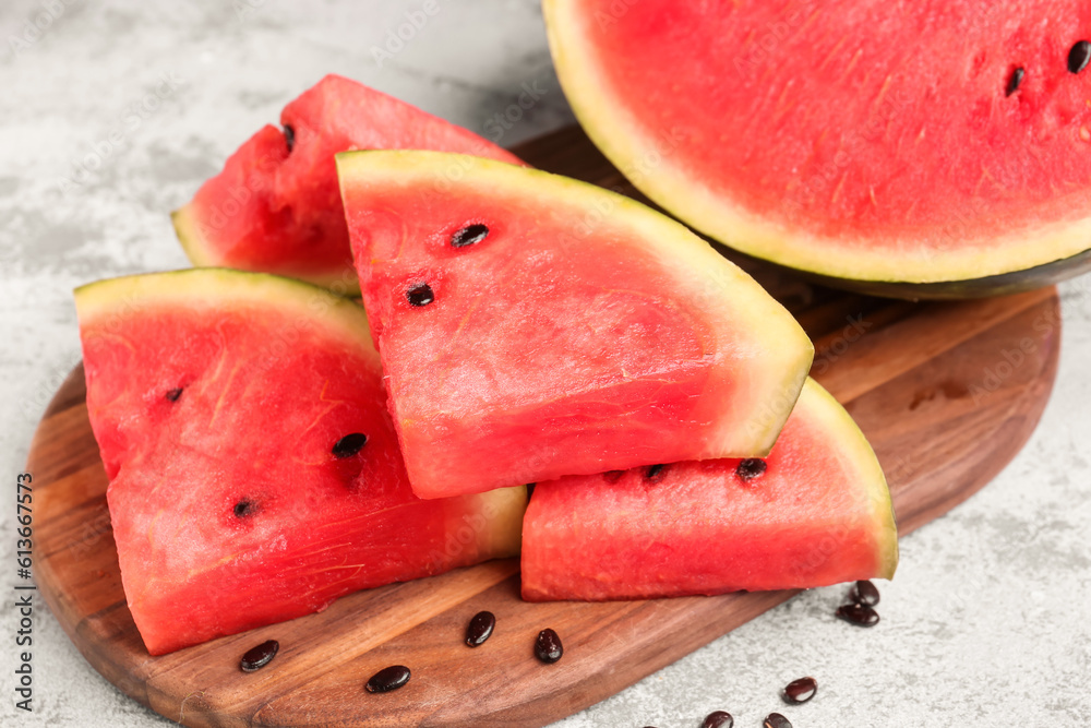 Board with pieces of fresh watermelon and seeds on grey background