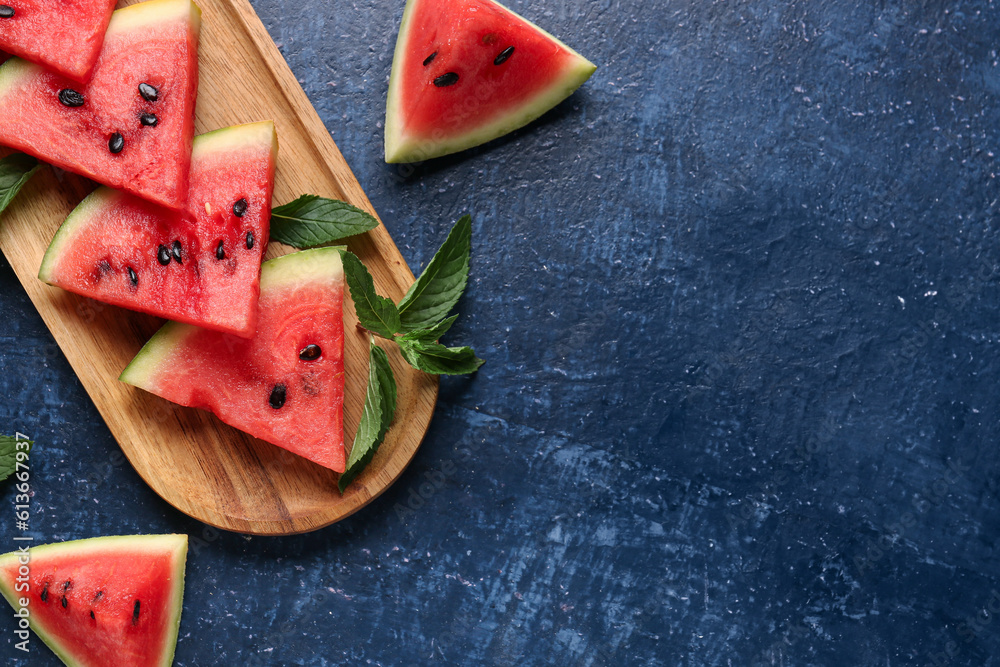 Board with pieces of fresh watermelon and mint on blue background