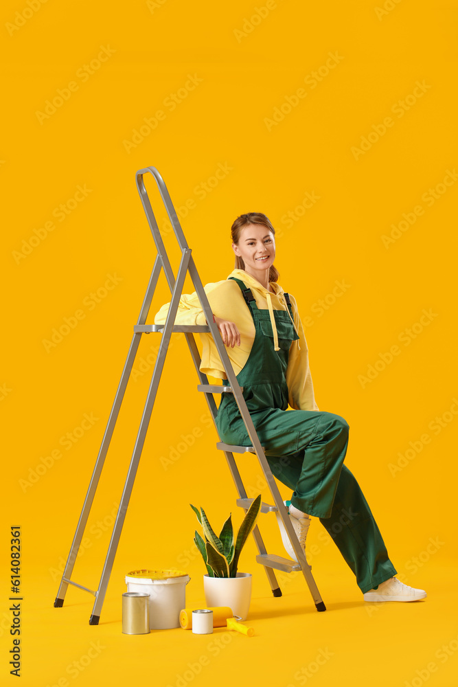 Young woman with ladder, houseplant and paint cans on yellow background