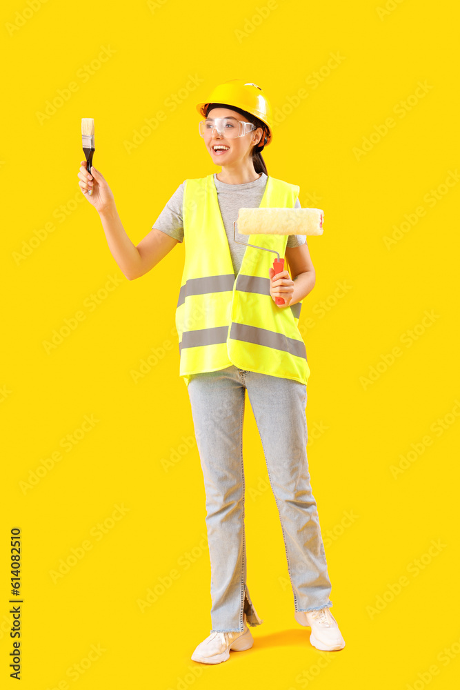 Female decorator with paint roller and brush on yellow background