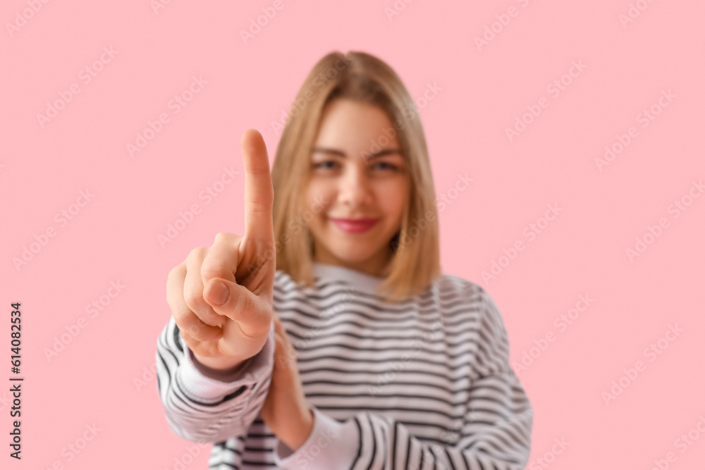 Young woman in striped sweatshirt showing one finger on pink background, closeup