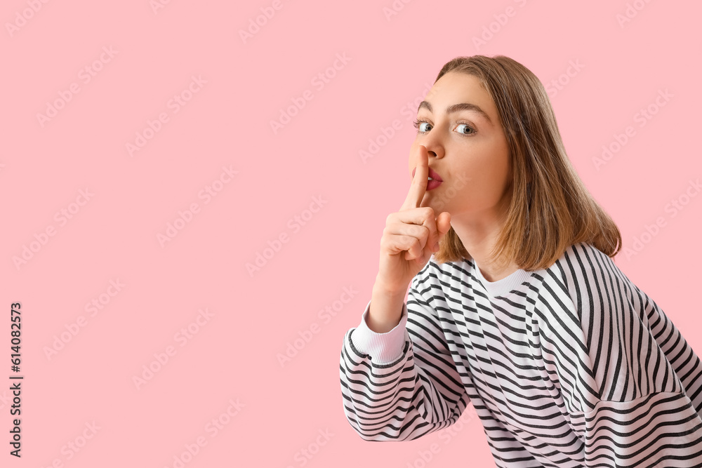 Young woman in striped sweatshirt showing silence gesture on pink background