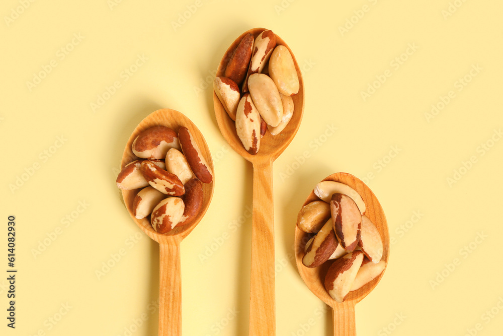 Wooden spoons of tasty Brazil nuts on yellow background, closeup