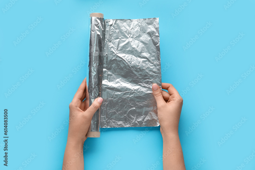 Female hands with roll of aluminium foil on color background