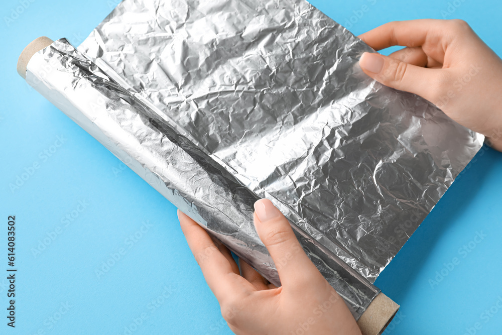 Female hands with roll of aluminium foil on color background, closeup