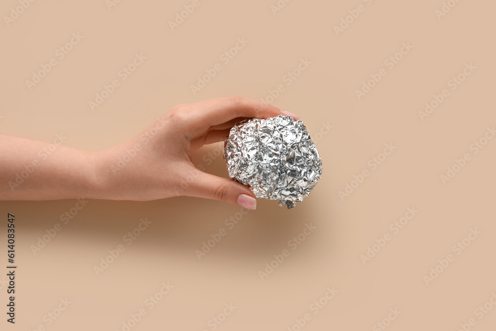 Female hand with aluminium foil ball on color background