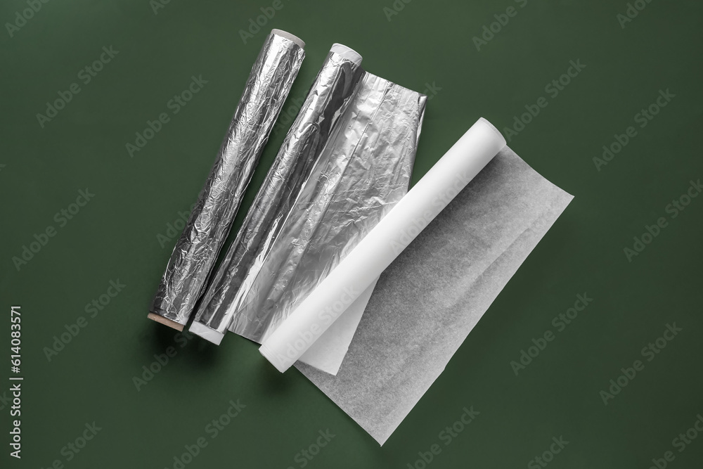 Rolls of aluminium foil and baking paper on color background