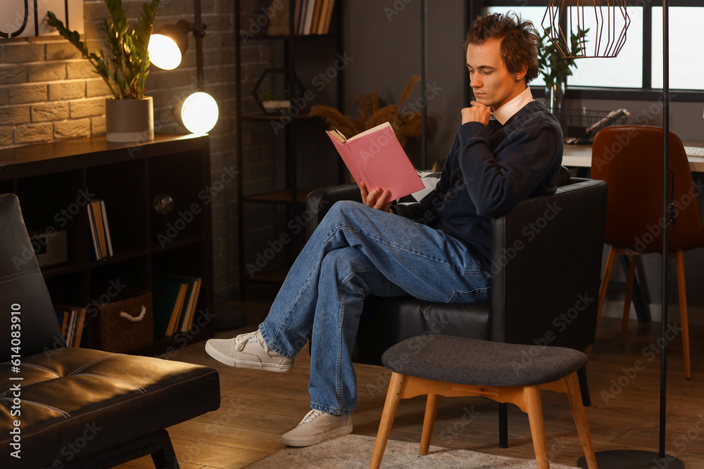 Young man reading book at home late in evening