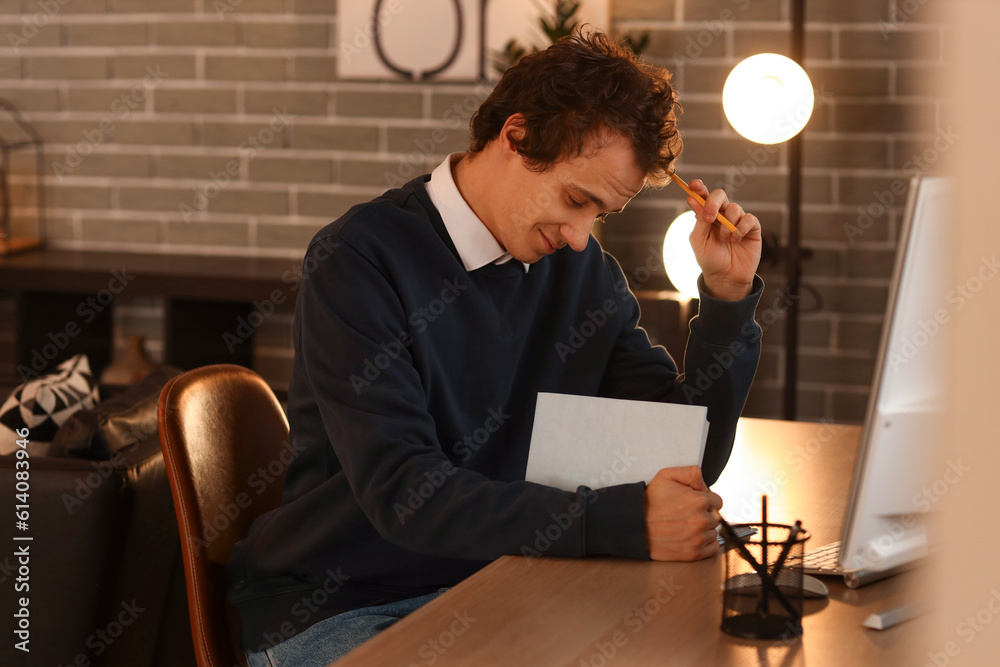 Young man reading book at table late in evening