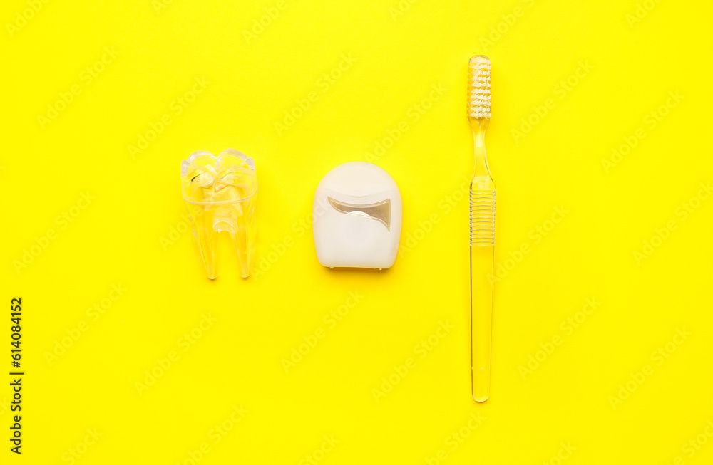 Dental floss, plastic tooth model and brush on yellow background