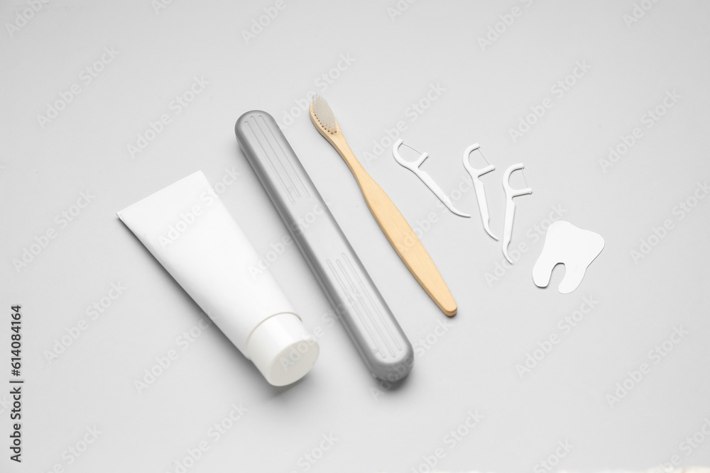 Floss toothpicks, tube of paste, brush and tooth model on grey background