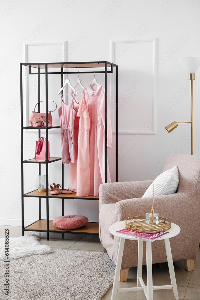 Interior of light room with shelving unit, clothes and armchair