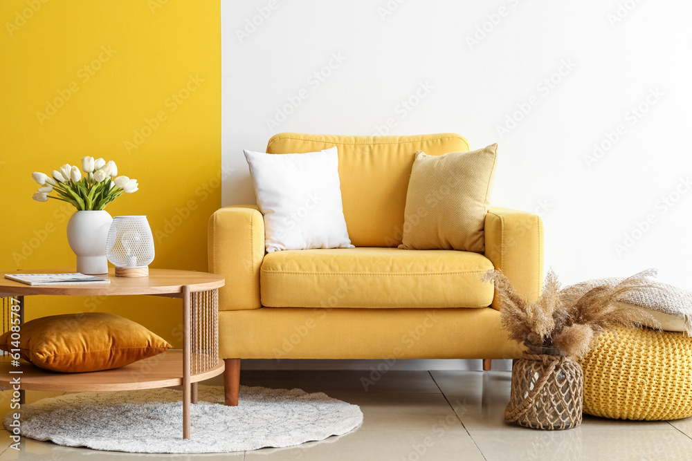 Cozy armchair and coffee table with tulip flowers in vase near colorful wall