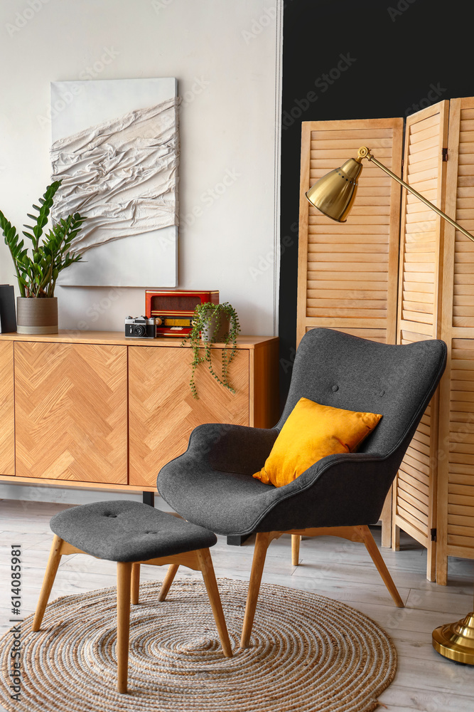 Cozy grey armchair with footstool in interior of living room