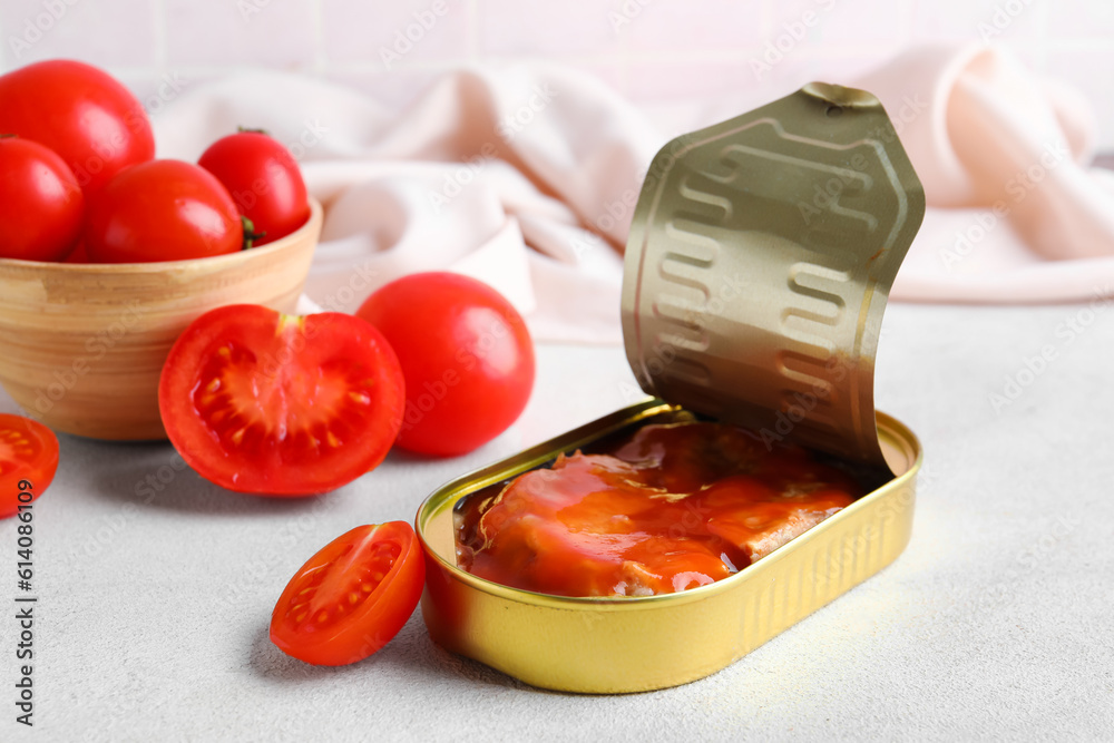 Opened can with fish in sauce and tomatoes on white table