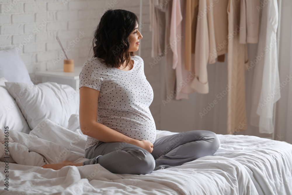 Young pregnant woman sitting in bedroom