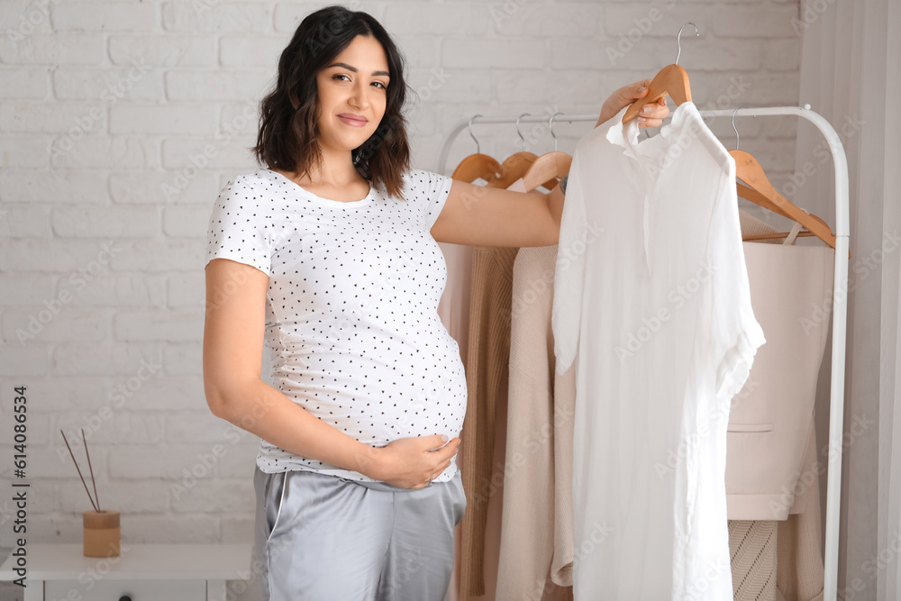 Young pregnant woman with clothes in bedroom