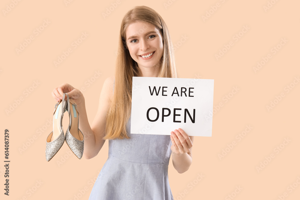 Young woman with shoes and opening sign on beige background