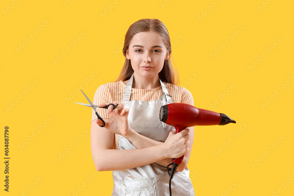 Female hairdresser with dryer and scissors on yellow background