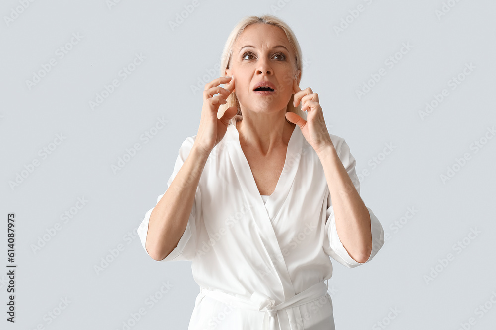 Mature woman doing face building exercise on light background