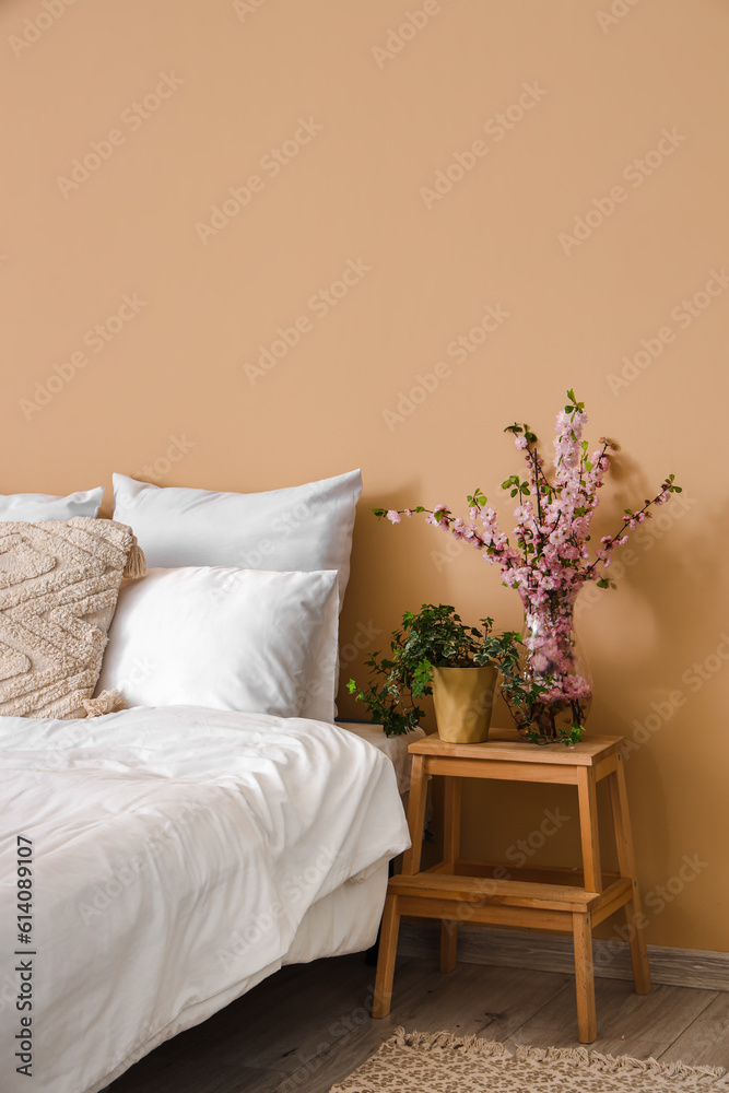 Vase with blooming sakura branches on step ladder near bed