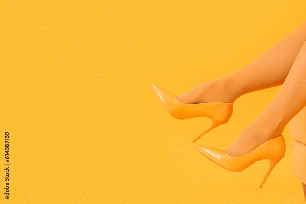 Female legs in high heels on sofa against yellow background