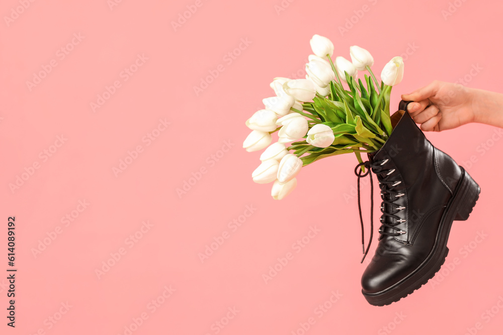 Female hand with tulip flowers in shoes on pink background