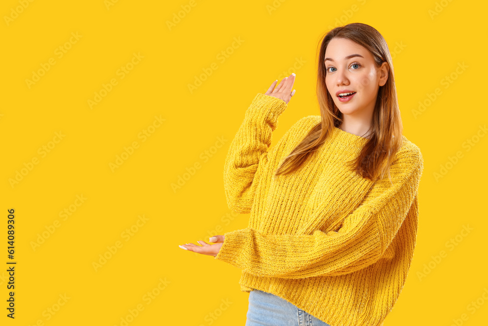 Beautiful young woman showing something on yellow background