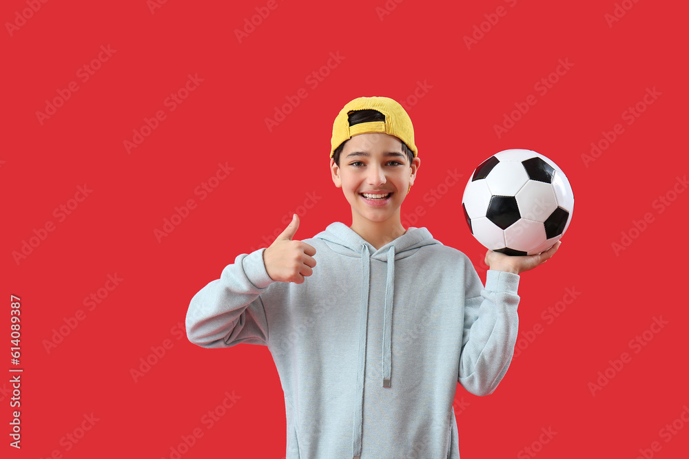 Little boy with soccer ball showing thumb-up on red background