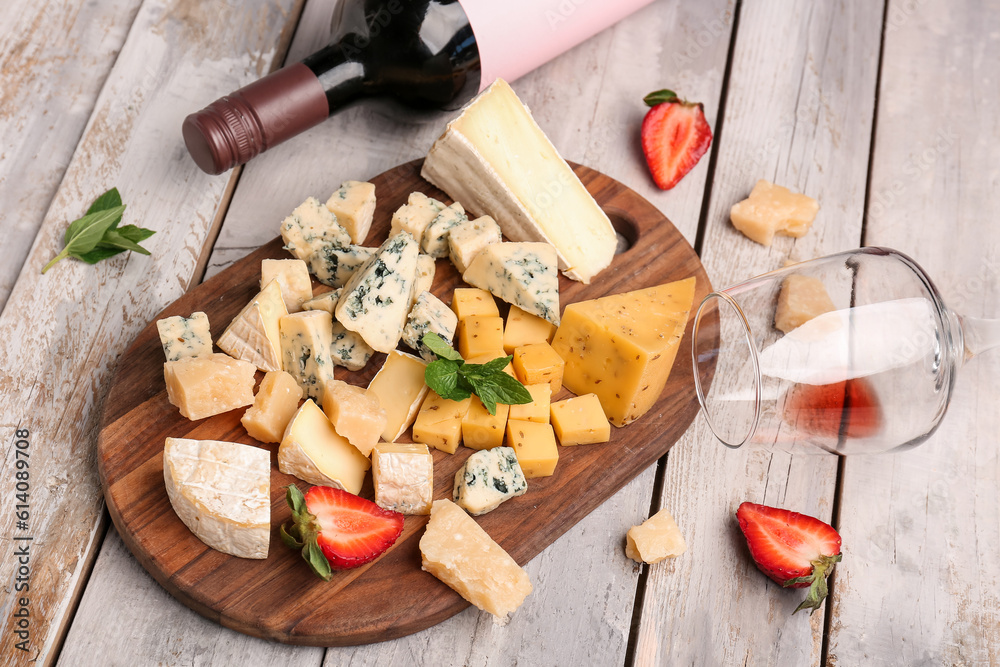 Pieces of tasty cheese, glass and bottle with wine on light wooden background