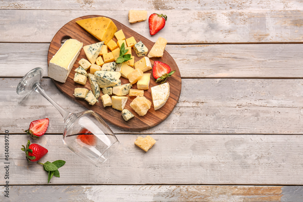 Board with pieces of tasty cheese and wine glass on light wooden background