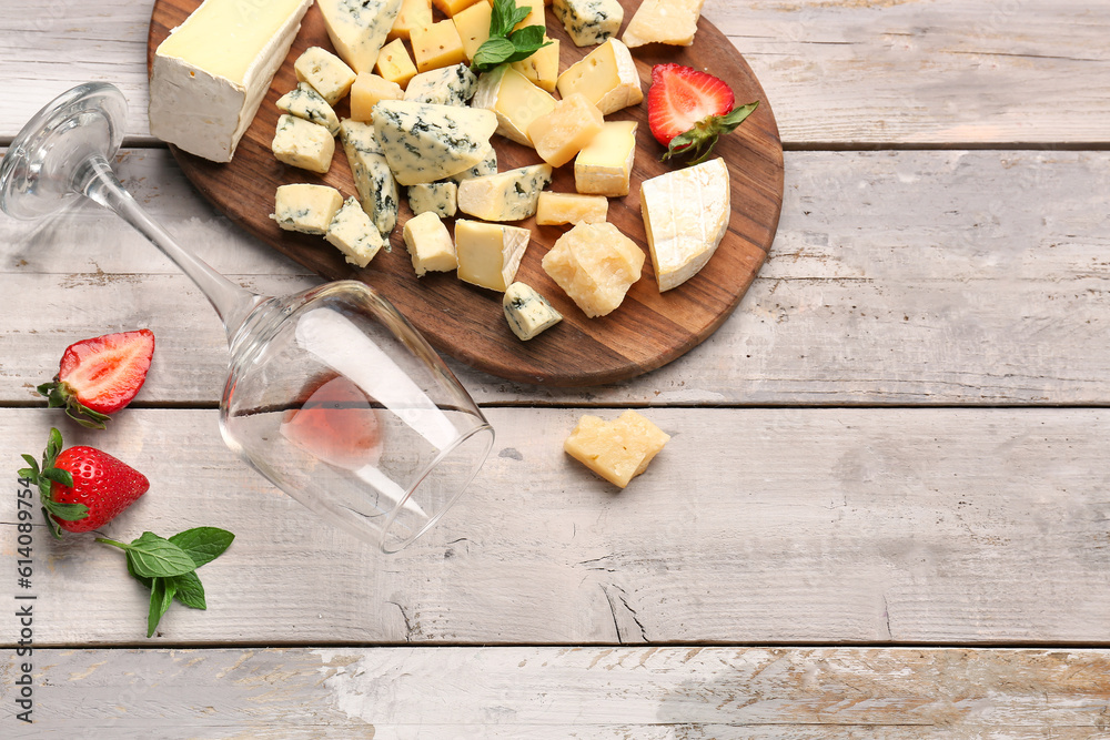 Board with pieces of tasty cheese and wine glass on light wooden background