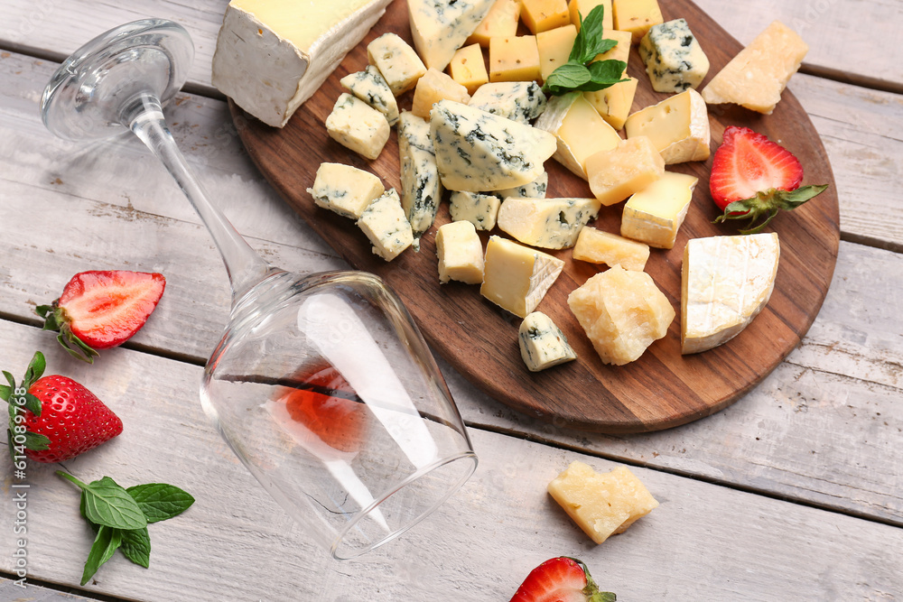 Board with pieces of tasty cheese and wine glass on light wooden background