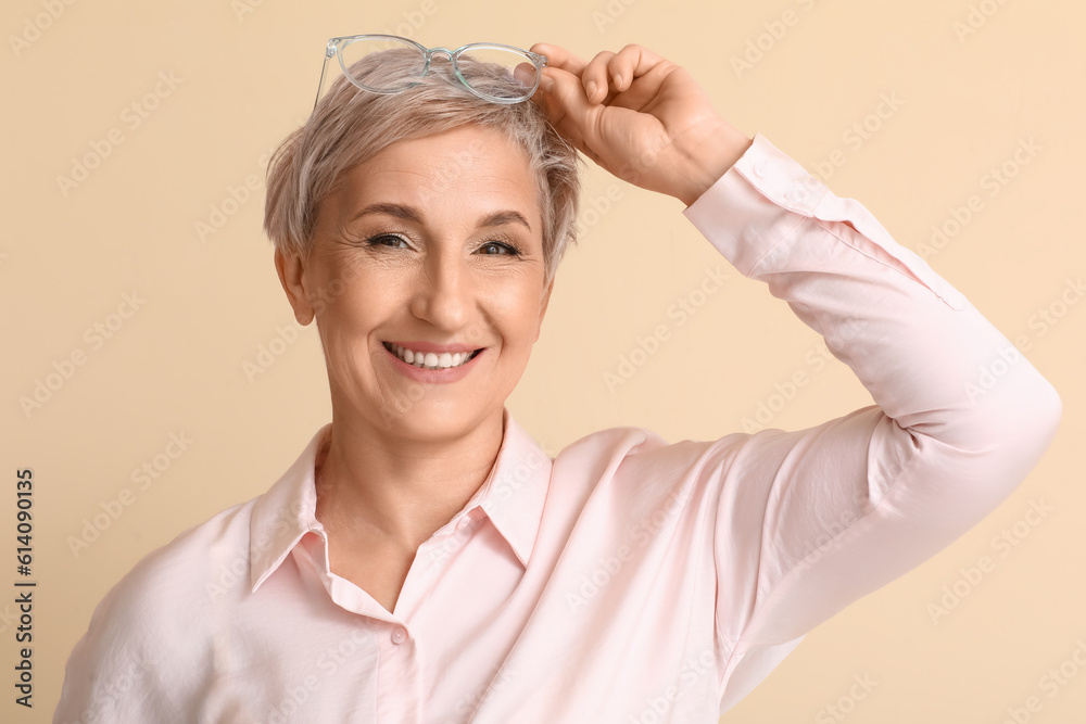 Mature blonde woman with eyeglasses on beige background, closeup