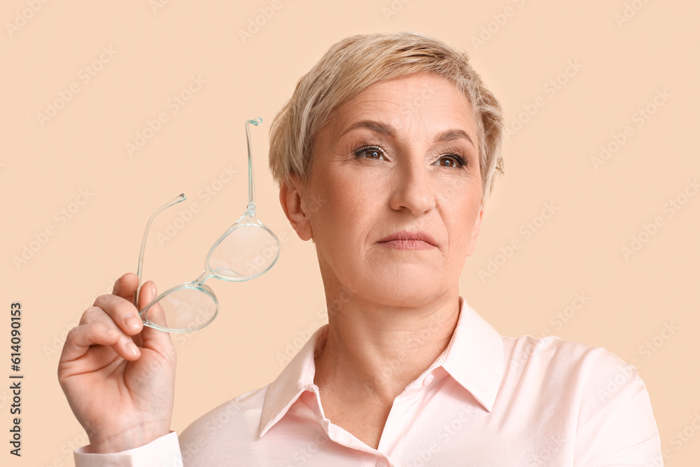 Mature blonde woman with eyeglasses on beige background, closeup