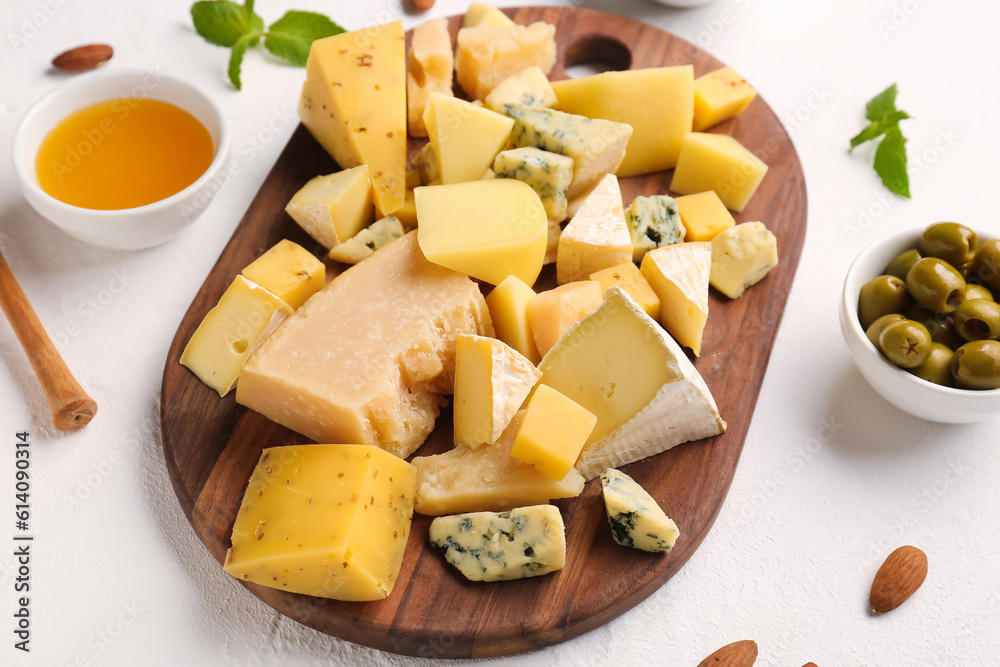 Wooden board with pieces of tasty cheese on light background