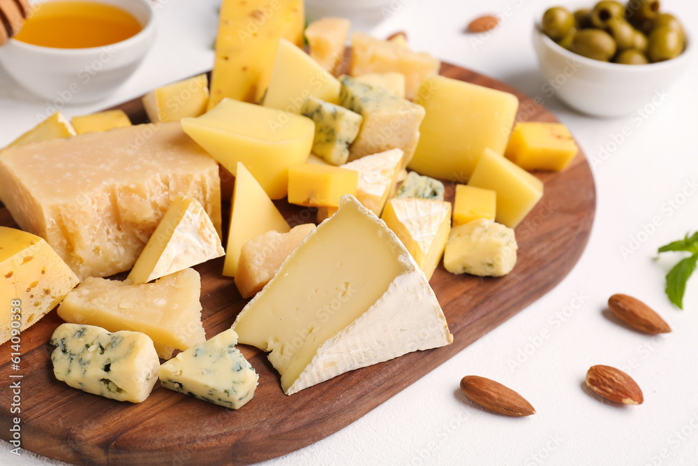 Wooden board with pieces of tasty cheese on light background