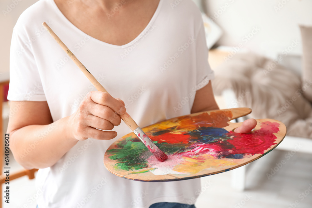 Mature female artist with palette and brush in  workshop, closeup