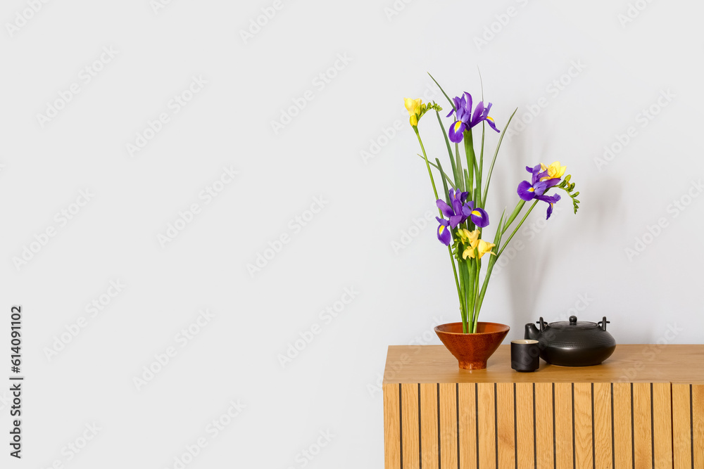 Beautiful ikebana with teapot and cup on table near light wall