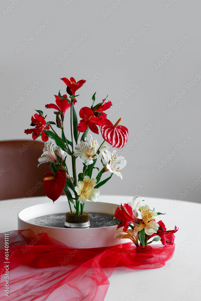 Beautiful ikebana with red veil on dining table in room