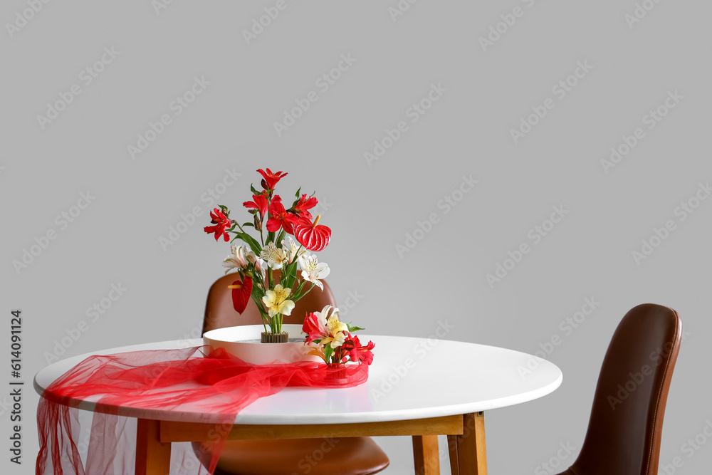 Beautiful ikebana with red veil on dining table in room