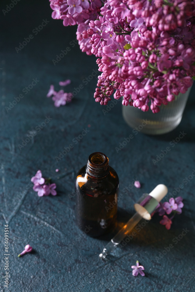 Bottle of cosmetic oil with beautiful lilac flowers on dark table