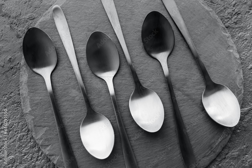 Board with stainless steel spoons on black background