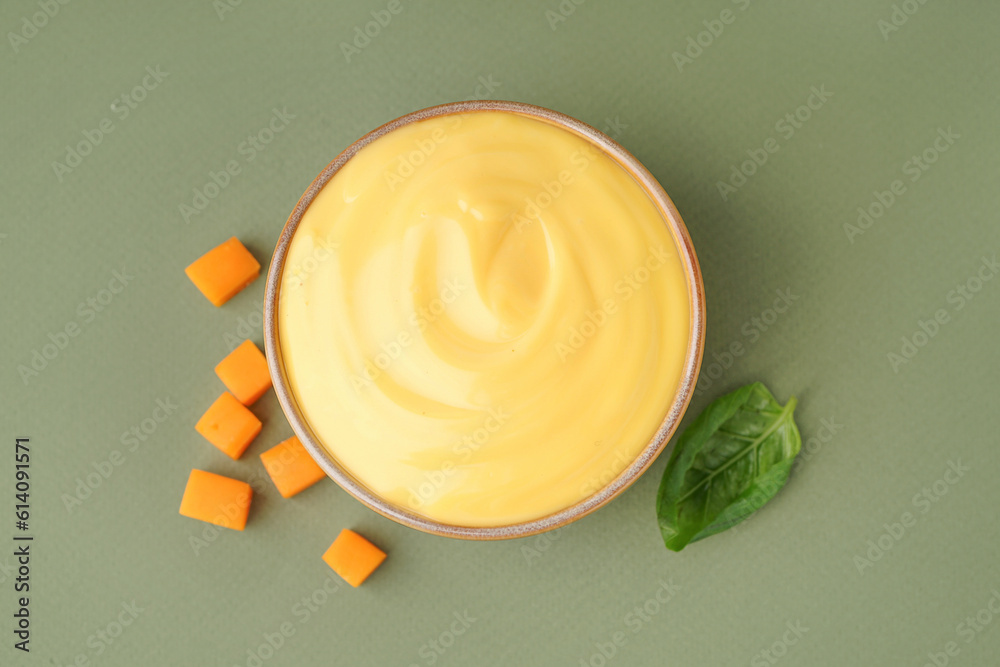 Bowl of tasty cheddar sauce with cheese cubes on green background