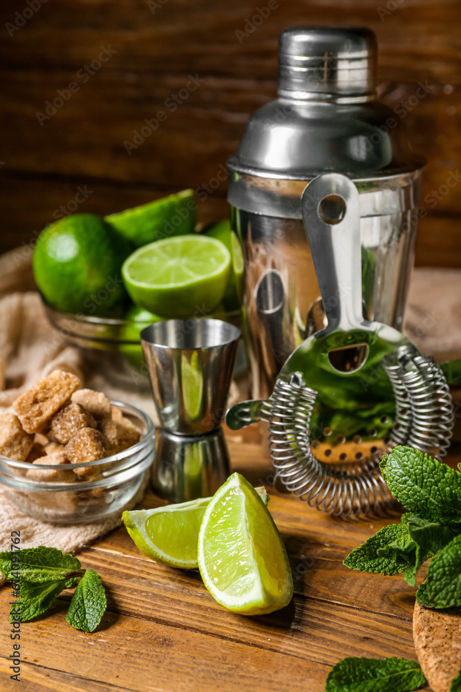 Shaker, strainer and ingredients for preparing mojito on wooden background