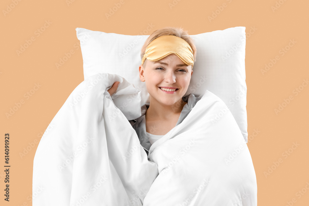 Young woman with pillow and blanket on beige background