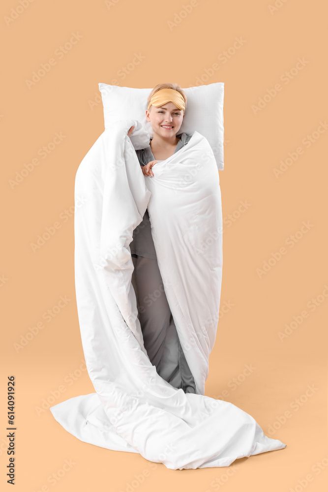 Young woman with pillow and blanket on beige background